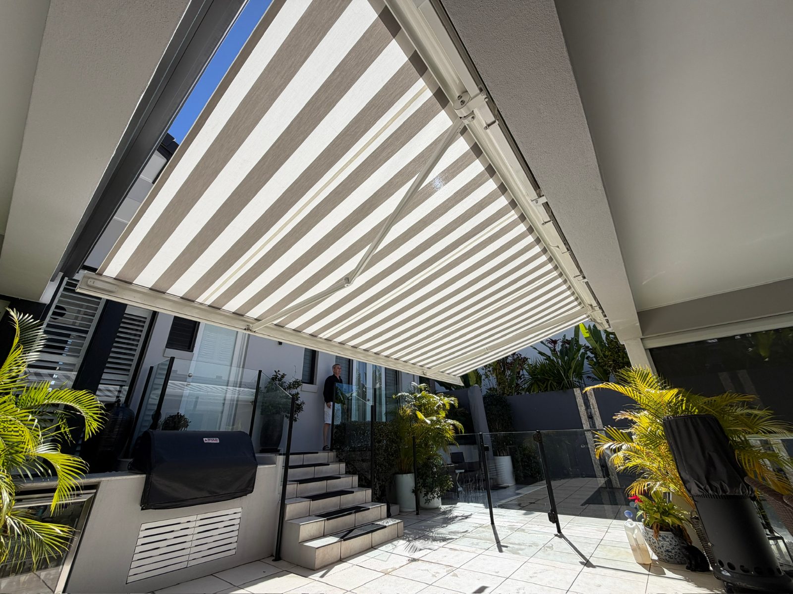 Siena full cassette folding arm awning with beige striped acrylic fabric extended over a poolside alfresco area in Bokarina, Sunshine Coast